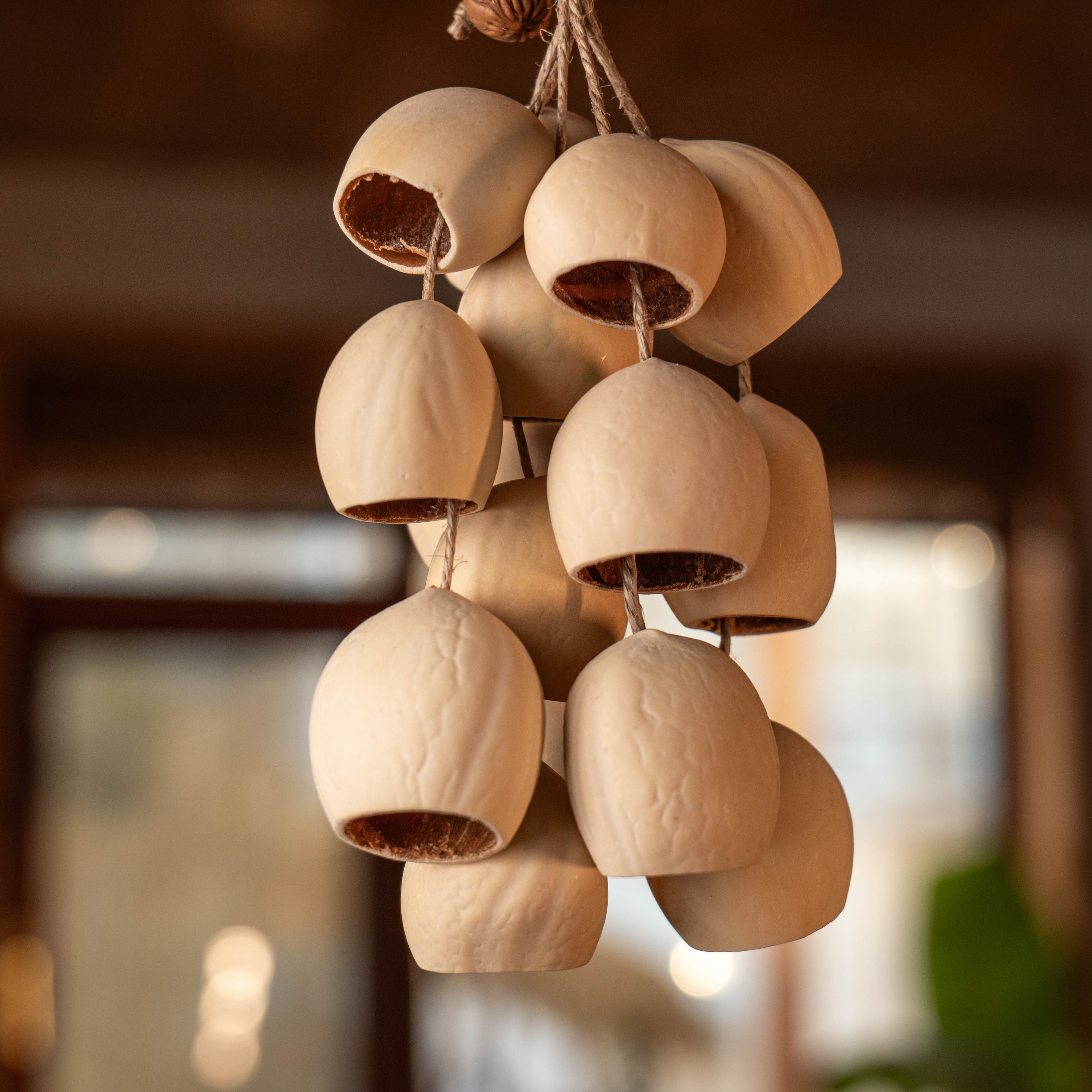 Handcrafted bag charm featuring 15 cream-colored Phoenix Egg botanical shells with a peach pit accent and hand-woven loop