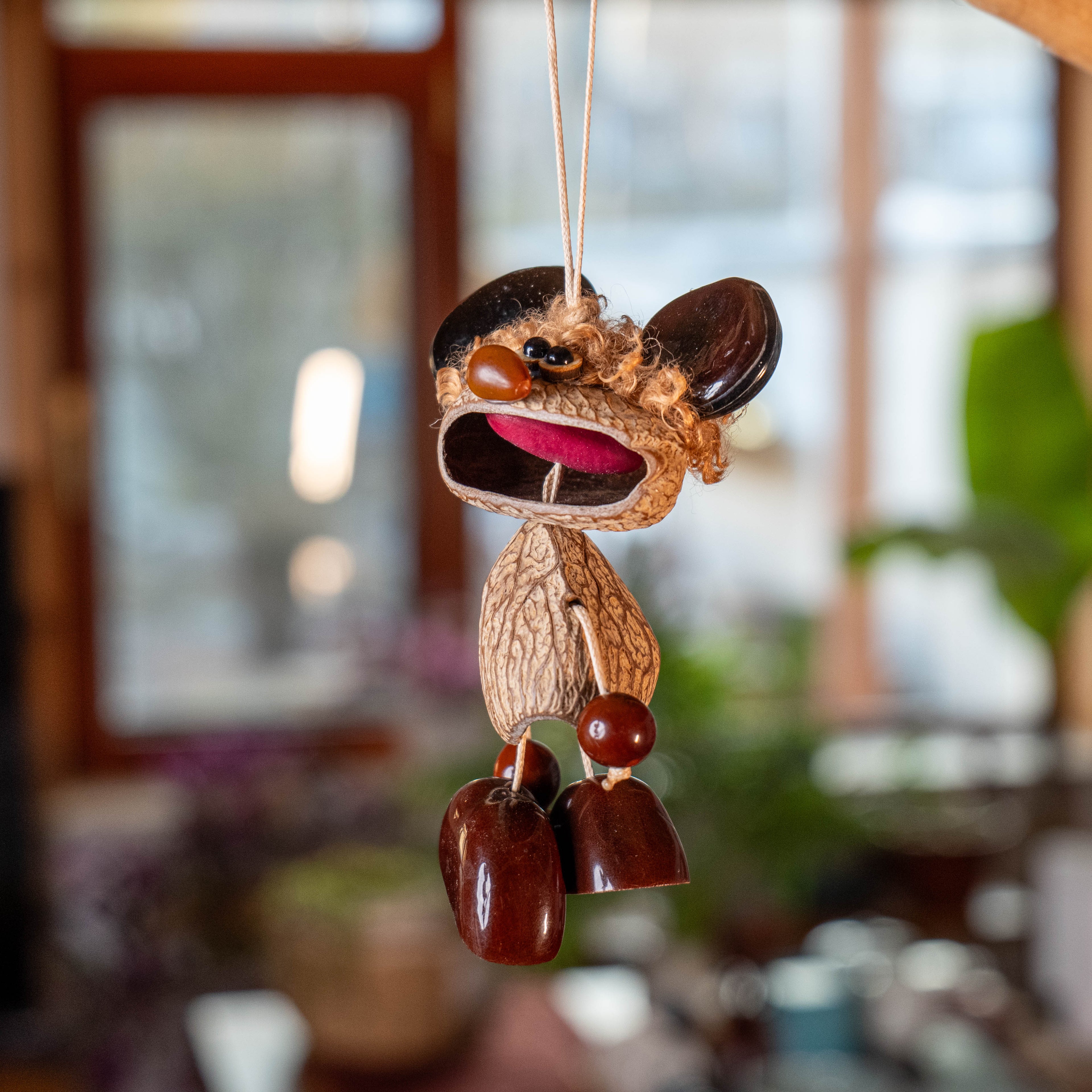 Handcrafted quirky bag charm puppet made from natural nut shells and botanical seeds, featuring a whimsical expression and earthy textures